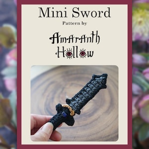 Può includere: Un documento con schema per uncinetto di una mini spada intitolato Mini Sword Pattern by Amaranth Hollow. L'immagine mostra una piccola spada lavorata all'uncinetto in nero e grigio con un dettaglio ad anello dorato e un piccolo accento quadrato blu sull'elsa.