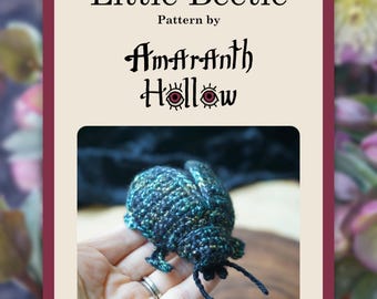 Op de afbeelding: Een gehaakte kever in tinten van blauwgroen, blauw en zwart, met fijne antennes en poten. De afbeelding is omlijst door een bordeauxrode rand en bevat de tekst "Little Beetle" en "Pattern by Amaranth Hollow".