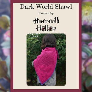 Puede incluir: Un chal de ganchillo magenta con un borde azul está drapeado sobre los hombros de una persona. El chal forma parte del patrón "Dark World Shawl" de Amaranth Hollow. La imagen está enmarcada por un borde rojo oscuro e incluye texto en la parte superior.