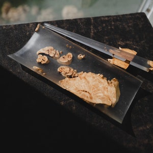 May include: A clear resin tray and chopsticks set with embedded wood pieces. The tray has a rectangular shape with rounded corners. The chopsticks are partially encased in clear resin. The wood pieces have a light brown colour.