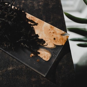 May include: A close-up of a small, rectangular tray made of clear resin with a wood inlay. The tray is filled with loose leaf black tea.