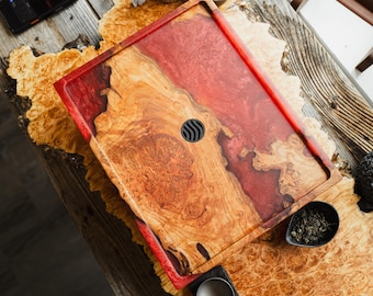 Puede incluir: Una bandeja de servicio rectangular hecha de madera de raíz de color marrón claro natural y resina roja translúcida. La bandeja presenta una superficie lisa y pulida con un inserto de drenaje negro circular en el centro y un borde elevado.