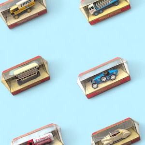 May include: A selection of miniature toy vehicles presented in display cases. The collection features a yellow Fyffes truck, a blue truck, a double-decker bus, a blue race car, a red Conoco tanker, and a cream-colored convertible.