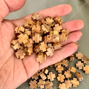 Könnte beinhalten: Ein Haufen kleiner Holzkreuzperlen aus Olivenholz, mit einem Loch, das durch die Mitte jedes Kreuzes gebohrt ist. Die Perlen sind hellbraun und haben eine natürliche Holzmaserung.