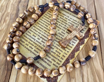 Può includere: Rosario in legno di ulivo con un cordino marrone e una croce in legno. Le perle sono marroni e hanno una venatura naturale del legno. La croce è scolpita con un design dettagliato. Il rosario è accompagnato da un certificato di conformità di Holy Land Point LTD, uno studio e laboratorio di legno di ulivo a Betlemme, Palestina. Il certificato indica che il prodotto è realizzato da artigiani di Betlemme e che il legno di ulivo proviene dalla Terra Santa. Il certificato include anche una descrizione del legno di ulivo e delle sue qualità uniche.