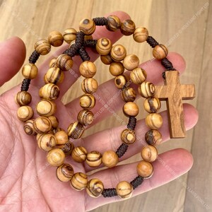 May include: A brown wooden rosary with a brown wooden cross. The beads are made of olive wood and have a striped pattern.