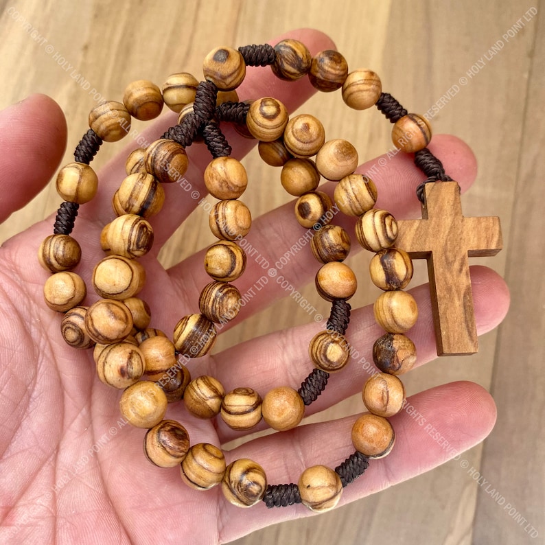 May include: A brown wooden rosary with a brown wooden cross. The beads are made of olive wood and have a striped pattern.