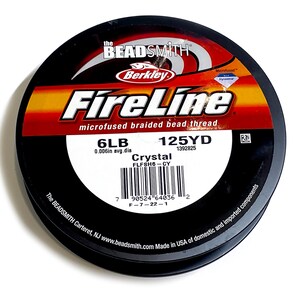 May include: A spool of black FireLine microfused braided bead thread, with a label that reads "6LB 0.006in avg. dia 125YD 1392825 Crystal FLFSH6-CY" and a barcode. The label also includes the text "The BEADSMITH Carteret, NJ www.beadsmith.com Made in USA of domestic and imported components."