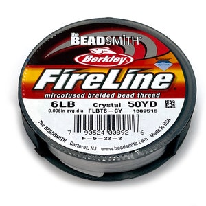 May include: A spool of white FireLine microfused braided bead thread by Berkley. The spool is labeled with the text "FireLine", "mircofused braided bead thread", "6LB", "Crystal 50YD", "0.006in avg.dia FLBT6-CY 1389515", "The BEADSMITH Carteret, NJ www.beadsmith.com Made in USA" and a barcode.