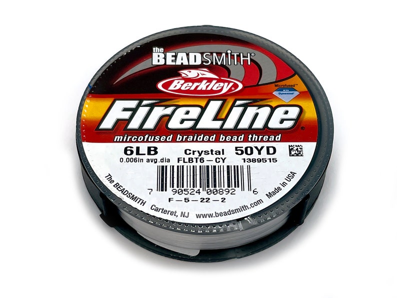 May include: A spool of white FireLine microfused braided bead thread by Berkley. The spool is labeled with the text "FireLine", "mircofused braided bead thread", "6LB", "Crystal 50YD", "0.006in avg.dia FLBT6-CY 1389515", "The BEADSMITH Carteret, NJ www.beadsmith.com Made in USA" and a barcode.