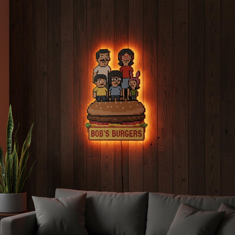 May include: Pixelated wall art featuring the Bob's Burgers family standing on a burger. The sign below the burger reads "BOB'S BURGERS". The art is illuminated with an orange glow against a dark wood background.