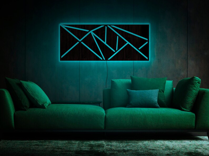 May include: A dark wood wall art piece with a geometric design, illuminated with a bright blue light. The art is hanging above a green sofa with pillows.