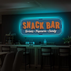 May include: A blue and white neon sign with the text "Snack Bar" in orange letters. The sign also includes the text "Drinks, Popcorn, Candy" in smaller orange letters.