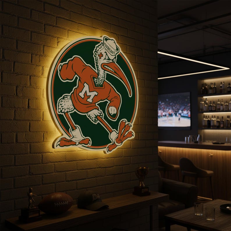 May include: A lighted wall sign featuring a cartoon pelican in an orange jersey with the letter "M" on a green circle. The pelican wears a sailor hat. The sign is mounted on a brick wall.