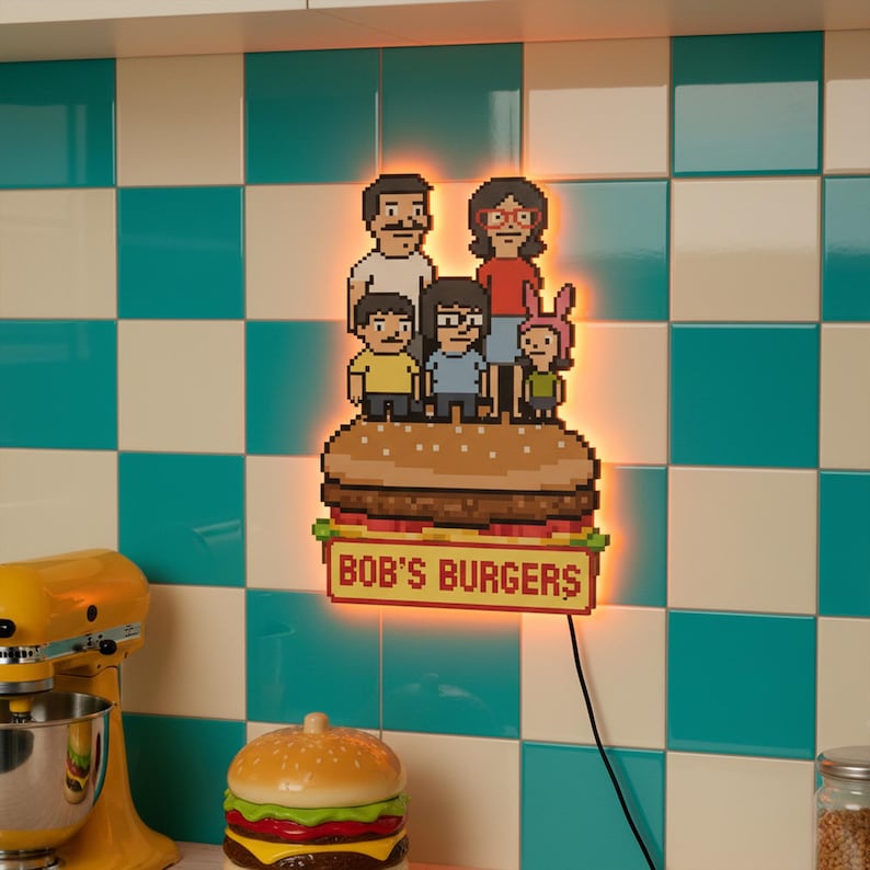 May include: A pixelated light-up sign featuring the Bob's Burgers family atop a burger. The sign has a warm orange glow and the text "BOB'S BURGERS" at the bottom. The background is a teal and white checkered pattern.