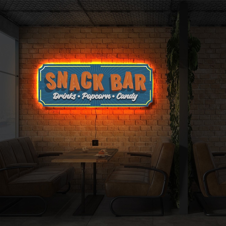 May include: A blue and orange neon sign with the text "Snack Bar" and the words "Drinks, Popcorn, Candy" underneath. The sign is mounted on a brick wall in a dimly lit room with a table and chairs.