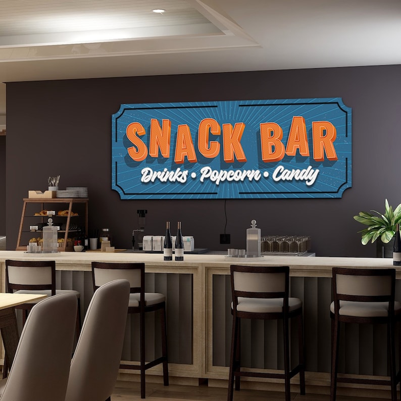 May include: A blue and orange sign with the text "Snack Bar" and the words "Drinks, Popcorn, Candy" underneath. The sign is hanging on a wall above a bar counter with stools.