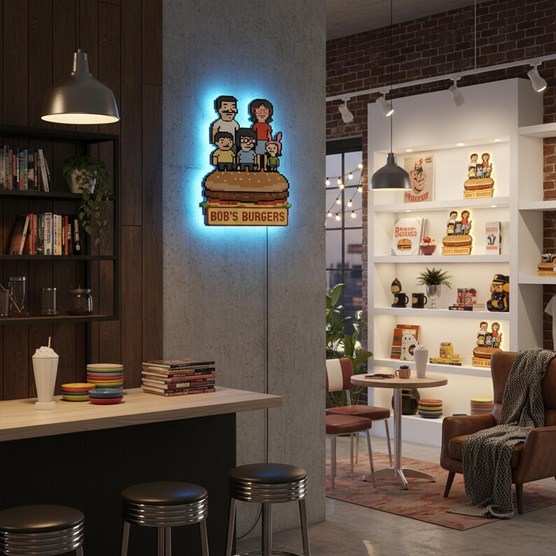 May include: A lighted wall art piece featuring the Bob's Burgers family atop a pixelated burger. The sign has a blue neon glow and the text "BOB'S BURGERS" below the burger. The art is mounted on a gray concrete wall.