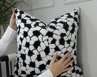 Puede incluir: Una almohada de tiro con estampado en blanco y negro con un diseño geométrico. La almohada está siendo sostenida por una mano.