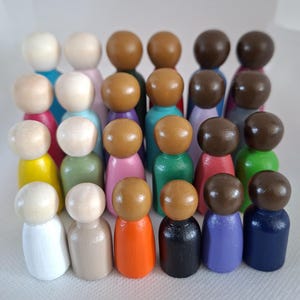 May include: A collection of twenty-four wooden peg dolls arranged in four rows. Each figure features a smooth, rounded head and a cylindrical body painted in a variety of solid colours, including white, yellow, pink, green, orange, black, purple, and blue.