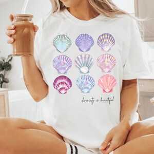 May include: White t-shirt with a graphic of nine colorful seashells and the text "diversity is beautiful".