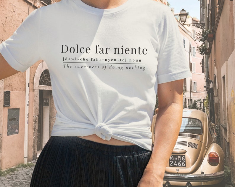 May include: White t-shirt with the text "Dolce far niente" and the definition "[dawl-che fahr-nyen-tel noun The sweetness of doing nothing" printed on the front.