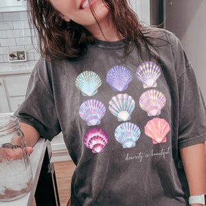 May include: A dark gray t-shirt with a graphic of colorful seashells and the text "diversity is beautiful".