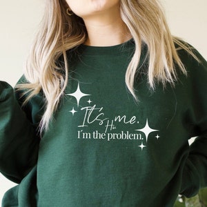 May include: A dark green sweatshirt with white text that reads "It's me. I'm the problem." with small white stars around the text.