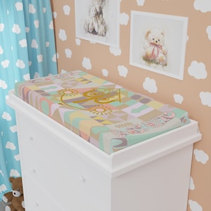 May include: A white changing table with three drawers and a changing pad with a colorful geometric pattern featuring a gold carriage and the text "Once Upon A Time".