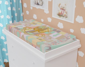 Op de afbeelding: Een witte commode met drie laden en een verschoningsmat met een kleurrijk geometrisch patroon met een gouden koets en de tekst "Er was eens".