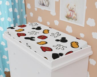Op de afbeelding: Witte verschoningsmatrashoes met een Mickey Mouse-print met rode, gele en zwarte Mickey Mouse-koppen en -handen.