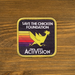 May include: Square patch with a yellow chicken graphic and the text "SAVE THE CHICKEN FOUNDATION" and "ACTIVISION" on a dark blue background. The patch has a yellow border and a rainbow-colored stripe design.