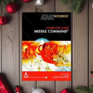 May include: A retro Atari Missile Command computer game box. The box features a black background with the game title in white and a vibrant illustration of a missile defense scene. The Atari logo is visible at the bottom.