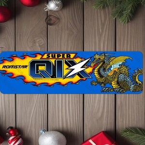 May include: A blue and yellow arcade game control panel with the text "SUPER QIX" and "ROMSTAR" in a yellow flame design. A gold dragon with blue scales is on the right side of the panel.