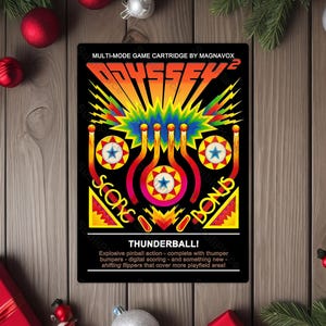 May include: A black game cartridge featuring the text "ODYSSEY 2" in orange and yellow, with a colorful graphic of a pinball machine. The cartridge includes the text "THUNDERBALL!" and game details.