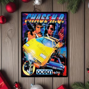 May include: A framed poster featuring the arcade game "Chase H.Q." The artwork depicts two men holding guns, a yellow sports car, and a blue car. The game's title is in blue and orange, with the Ocean and Taito logos at the bottom.