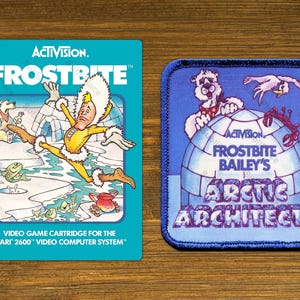 May include: Two vintage video game patches. The first is a teal rectangle with the game title "Frostbite" and a cartoon character. The second is a blue square patch with a polar bear and the text "Frostbite Bailey's Arctic Architects".