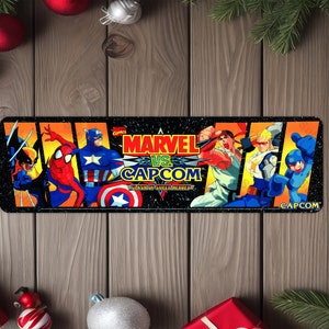 May include: A black and yellow arcade cabinet control panel with a colorful image of characters from the Marvel vs. Capcom video game. The image includes Wolverine, Spider-Man, Captain America, Ryu, Chun-Li, Captain Commando, and Mega Man. The text "MARVEL VS. CAPCOM" is displayed in the center of the image.