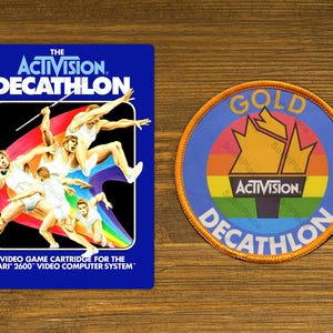 May include: A blue and orange video game cartridge for the Atari 2600 video computer system. The cartridge features a rainbow design with athletes competing in a decathlon. The text "THE ACTIVISION. DECATHLON" is printed on the front of the cartridge.