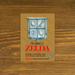May include: A rectangular, tan-colored card featuring the title "The Legend of Zelda" in red. A silver crest with a heart, key, and other symbols is at the top. The text "Includes invaluable maps and strategic playing tips" is below the title.