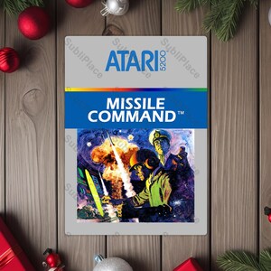 May include: A rectangular Atari 5200 game cartridge featuring the "Missile Command" game. The cartridge has a gray background with the Atari logo and game title in blue and white. The game art depicts a missile launch.