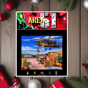 May include: A video game screen showing the title "AREA 51" with a helicopter flying over a military base. The game is set in a desert environment with a blue sky and white clouds. The text "PRESS START" is displayed on the screen.