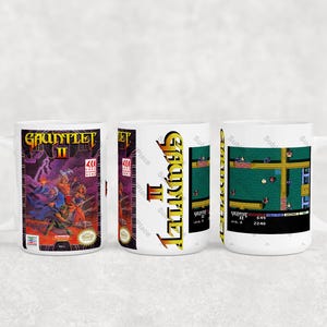 May include: White ceramic mug featuring the Gauntlet II video game. The mug displays the game's cover art, side art, and gameplay screenshots. The cover art shows characters in action with the game's title. The side art has the game's title in yellow. The gameplay screen shows a top-down view.