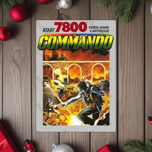 May include: Atari 7800 Commando video game cartridge. The cover art features a soldier in a combat scene with explosions and other soldiers. The game title is in large, bold, green and yellow letters.