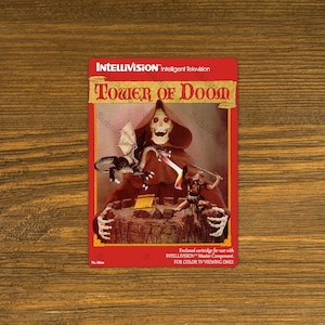 May include: A vintage Intellivision game cartridge box featuring a red-robed figure with a skull face holding a sword and a dragon. The box is titled "Tower of Doom" and is for use with the Intellivision Master Component.