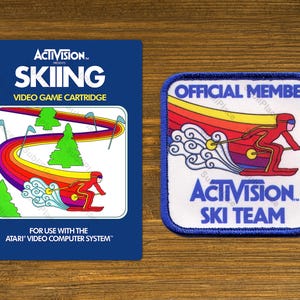 May include: A vintage Activision Skiing video game cartridge and a matching patch. The cartridge is dark blue with the game title and a skier graphic. The patch reads "Official Member" and "Activision Ski Team."