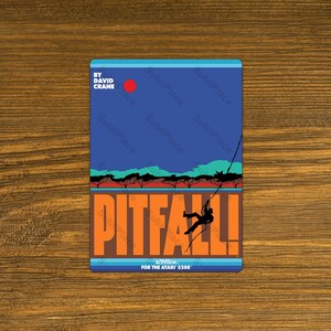 May include: A rectangular Pitfall! design featuring a blue sky with a red sun, a silhouette of trees, and the word "PITFALL!" in orange. The design includes the text "BY DAVID CRANE" and "FOR THE ATARI 5200".