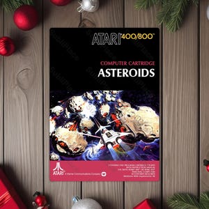 May include: A vintage Atari Asteroids video game cartridge. The cartridge features a black background with the game title and a spaceship illustration. The Atari logo is visible at the bottom. The cartridge is surrounded by Christmas decorations.