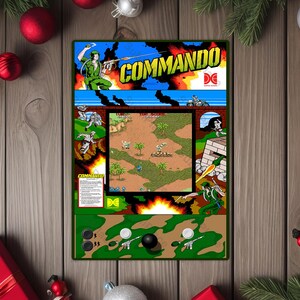 May include: A framed arcade game cabinet featuring the game "Commando." The cabinet has a green border and includes a joystick and buttons. The game's artwork depicts a soldier in action, explosions, and the game's title.