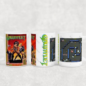 May include: White ceramic mug featuring artwork from the classic video game Gauntlet. The mug displays the game's logo and characters on one side, and a level map on the other. The word "Tengen" is also visible.